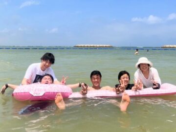 重度訪問介護の利用者様が家族旅行に行った写真です。沖縄の海で家族全員と弊社スタッフが写っています。